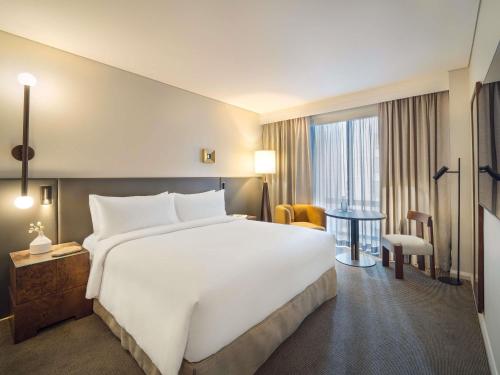 a hotel room with a large white bed and a table at Sofitel Sydney Wentworth in Sydney