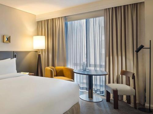 a hotel room with a bed and a table and a window at Sofitel Sydney Wentworth in Sydney