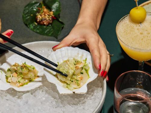 a woman holding a plate of food with chopsticks at Sofitel Sydney Wentworth in Sydney