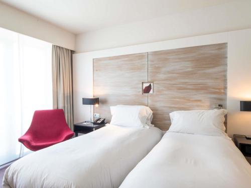 two beds in a hotel room with a red chair at Sofitel Brussels Europe in Brussels