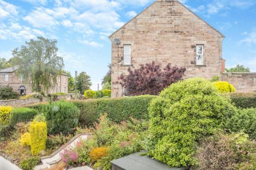 an old brick building with a garden in front of it at Lionels Den in Wooler