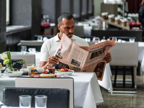a man sitting at a table reading a newspaper at Sofitel Munich Bayerpost in Munich