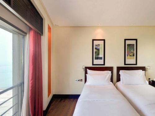 two beds in a room with a window at Sofitel Al Khobar The Corniche in Al Khobar