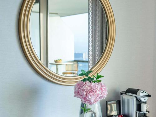 a vase with pink flowers in front of a mirror at Sofitel Dubai Jumeirah Beach in Dubai