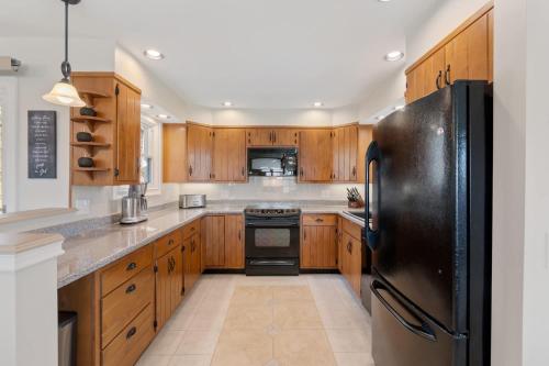 a kitchen with wooden cabinets and a black refrigerator at High-End Finger Lakes Escape - Expansive Game Room, Cozy Firepit, & Scenic Views in Penn Yan
