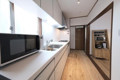 Una cocina blanca con fregadero y microondas. en KONODA HOUSE 成田空港車40分 貸切戸建 最大8名 駐車場2台完備Switch有, en Funabashi