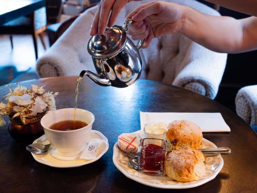 a person is pouring tea into a cup of coffee at Royal Emeraude Hotel Dinard - MGallery Collection in Dinard