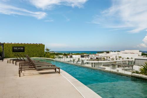 a resort pool with benches and the ocean in the background at The Shore by Stella in Playa del Carmen