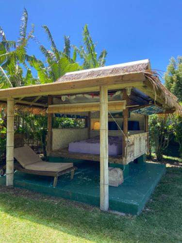 a wooden gazebo with a bed in the grass at Fare TEAK avec Palapa et piscine partagée in Maharepa