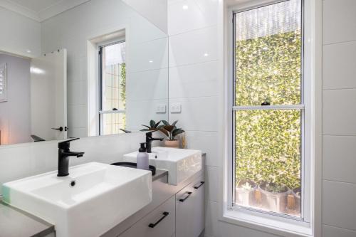 a white bathroom with two sinks and a window at Abode On Brookwater in Mollymook