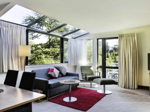 a living room with a couch and chairs and windows at Novotel Queenstown Lakeside in Queenstown
