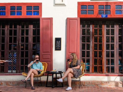 two people sitting in chairs in front of a building at 3 Nagas Hotel Luang Prabang - MGallery Collection in Luang Prabang