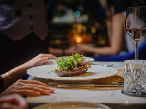 a table with a plate of food and a glass of wine at Hotel Des Arts Saigon Mgallery Collection in Ho Chi Minh City
