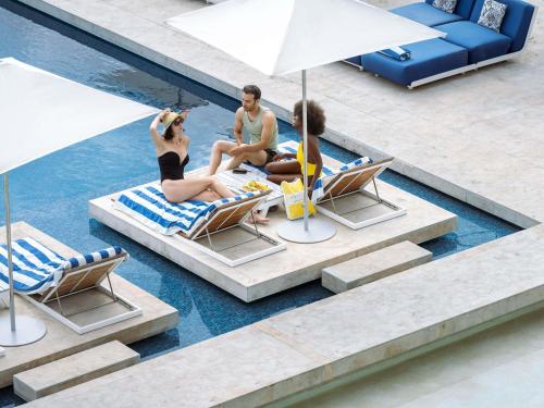 three people sitting on lounge chairs in a swimming pool at Sofitel Tamuda Bay Beach And Spa in M'diq