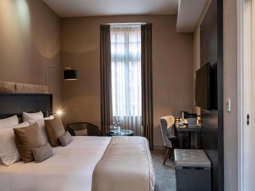 a bedroom with a bed and a desk and a window at La Cour des Consuls Hotel & Spa Toulouse - MGallery Collection in Toulouse