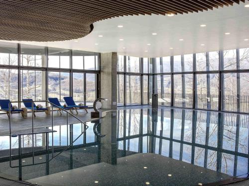 a large room with a pool with chairs and windows at Tarcin Forest Resort & Spa Sarajevo - MGallery Collection in Tarčin