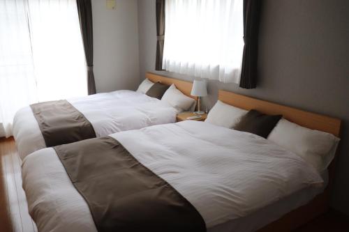 2 Betten in einem Schlafzimmer mit 2 Fenstern in der Unterkunft 飛梅の宿Tobiume inn in Dazaifu