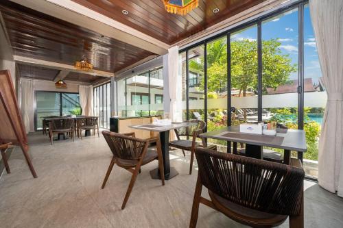 a dining room with tables and chairs and large windows at Howard Johnson by Wyndham Phuket Naiyang in Thalang