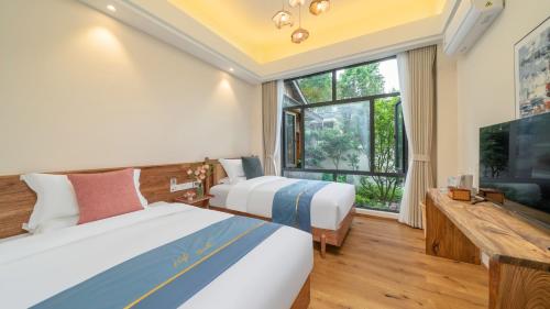 two beds in a room with a large window at Floral Hotel Tengchong Wuwenju B&B in Tengchong