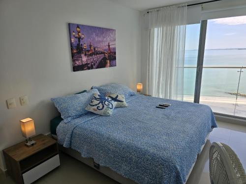 a bedroom with a bed with a blue comforter and a window at Ikigai frente al mar con piscina infinita y Gym in Cartagena de Indias