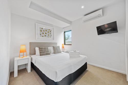 a white bedroom with a bed and a tv at Vine Apartments South Brisbane in Brisbane