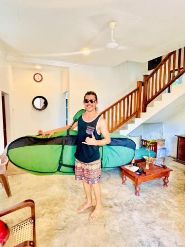 a man standing in a living room holding two surfboards at Coastal Cloud Backpackers Villa in Unawatuna