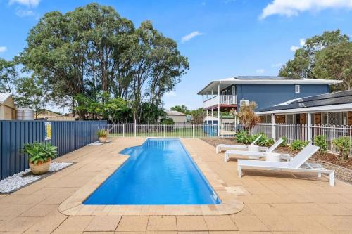 a swimming pool with lounge chairs and a house at Whitesands Family Beachhouse in Urangan