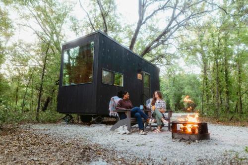 three people sitting on a bench next to a fire in front of a tiny house at Postcard Cabins Big Bear in Running Springs
