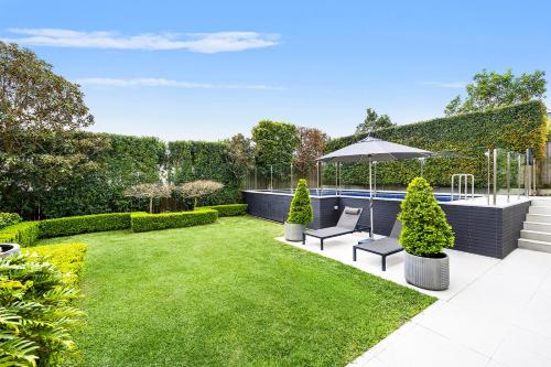 シドニーにあるKINGS10V - Luxe at Kingsのプールと芝生のある庭、椅子2脚とパラソル