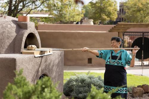a woman is holding a stick in front of a pizza oven at Hyatt Regency Tamaya South Santa Fe in Santa Ana Pueblo
