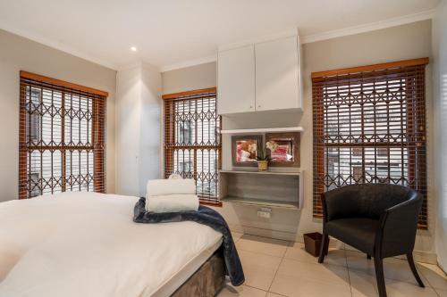 a bedroom with a bed and a chair and windows at Avemore Mareba Court No 9 in Stellenbosch