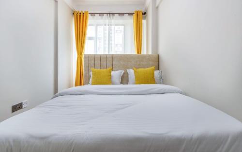 a white bed with yellow pillows and a window at Kilimani finest - One Bedroom Apartment in Nairobi