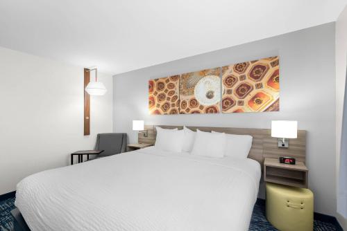 a hotel room with a white bed and a painting on the wall at Clarion Pointe in Shreveport