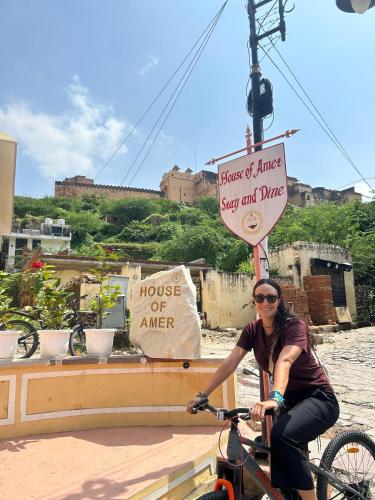 a woman riding a bike in front of a sign at House of Amer in Jaipur