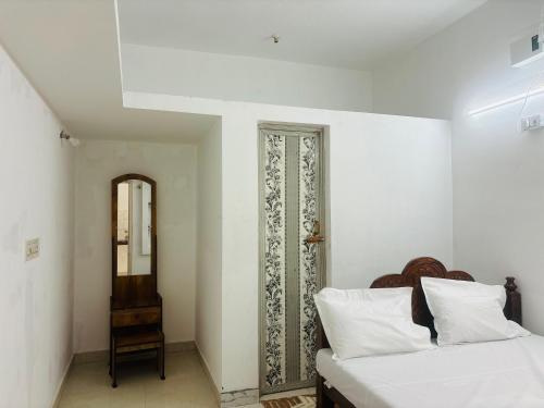 a white bedroom with a bed and a mirror at Chendur kumaran residency in Tiruchchendūr