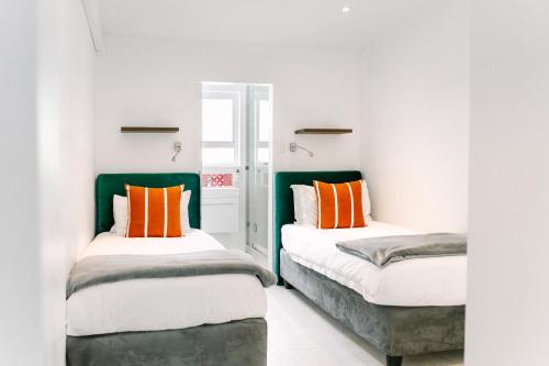 two beds in a room with white walls and orange pillows at The Salene Hotel & Apartments in Stellenbosch