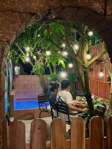 two people sitting at a table under a tree at Nhà Ven Hồ Đồng Đò, Minh Trí, Sóc Sơn, Hà Nội in Hanoi