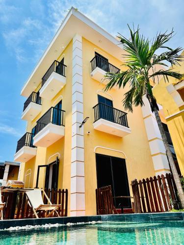 a yellow building with a palm tree and a swimming pool at Laa House in Hoi An
