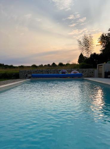 a large blue swimming pool with a sunset in the background at Le Petit Verger Gîte in Bonnes