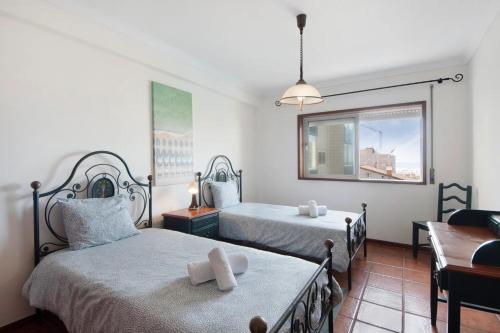 a bedroom with two beds and a chair and a window at Live Vagueira Beach in Praia da Vagueira