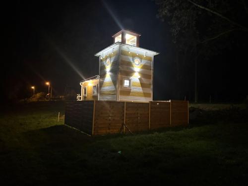 a clock tower at night with lights on it at Mazurska Latarnia z prywatną plażą i stawem in Rydzówka