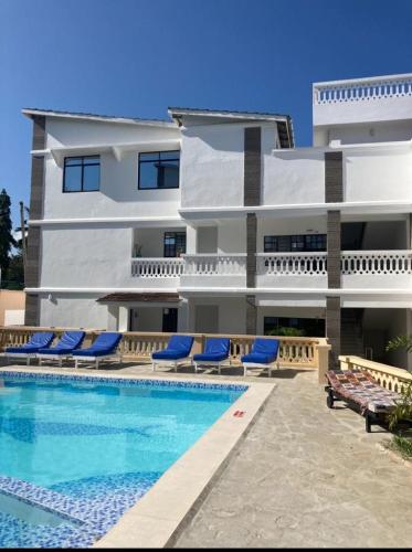 a building with a swimming pool and some blue chairs at Pamitos Sunny Paradise in Diani Beach in Diani Beach