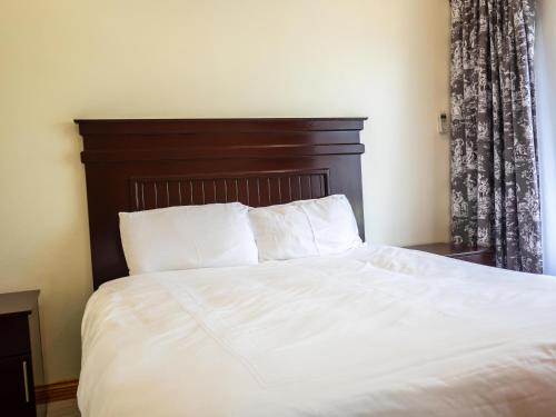a bedroom with a white bed with a wooden headboard at Apartments at Mombo in Blantyre