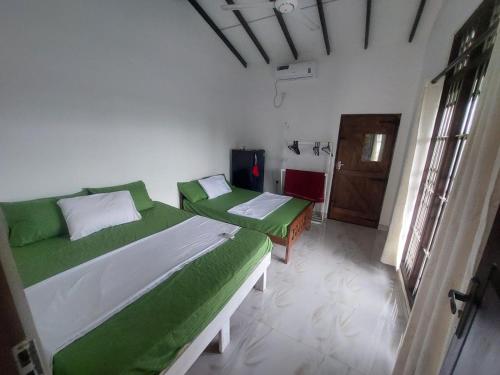 a bedroom with two beds with green sheets and a door at Hostel Lali beach villa in Trincomalee