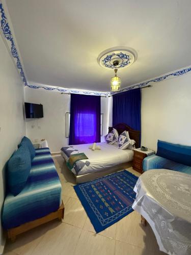 シェフシャウエンにあるDar Alamiのベッド2台とソファ、紫色のカーテンのある寝室
