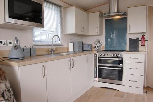 a kitchen with white cabinets and a sink and a stove at Premier Caravan 10 at The Vaenol, Tywyn in Tywyn