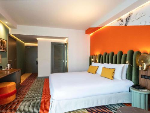 a bedroom with a large white bed with an orange wall at Mercure Shéhérazade Rabat in Rabat