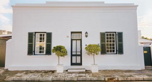 ein weißes Haus mit grünen Fensterläden und zwei Bäumen in der Unterkunft Karoo House Collection - 54 Middle in Graaff-Reinet