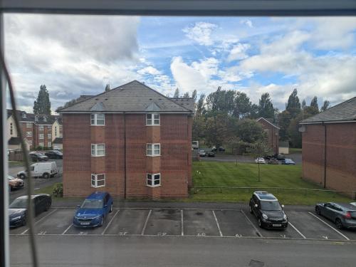 a large brick building with cars parked in a parking lot at Comfortable and Peaceful 2 Bedroom Flat with Shared Bathroom and Kitchen Close to Manchester Airport in Manchester