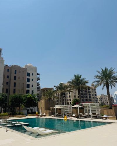 a swimming pool with chairs and palm trees and buildings at Rahaal 1 BDR, Madinat Jumeirah in Dubai